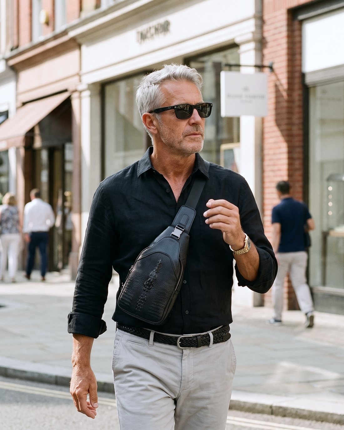 A grey-haired man in a black shirt on a shopping street, the CAIMAN sling across his chest